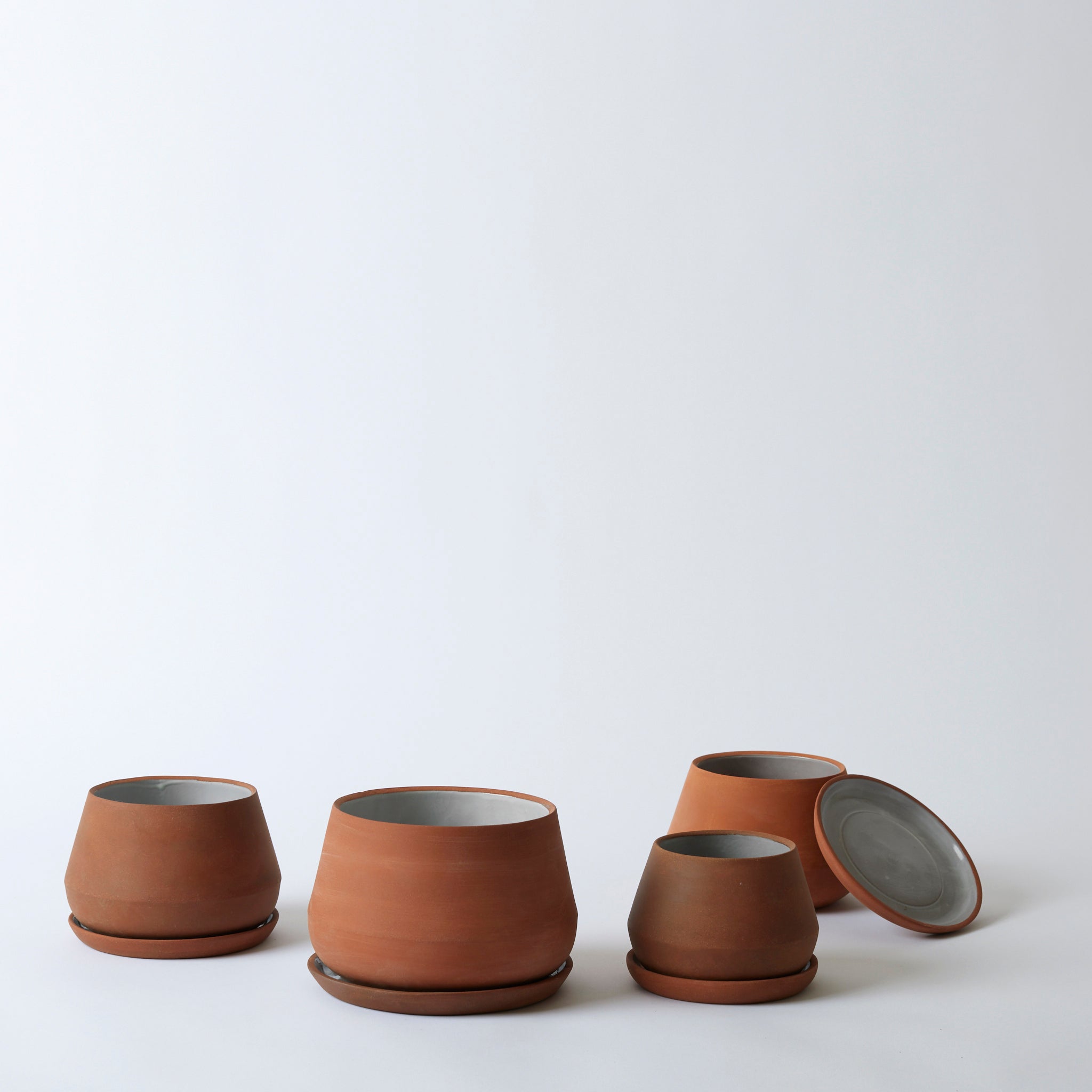 Group image of the terra cotta Rancho Planters in various sizes. One pot has its tray propped up on the planter.