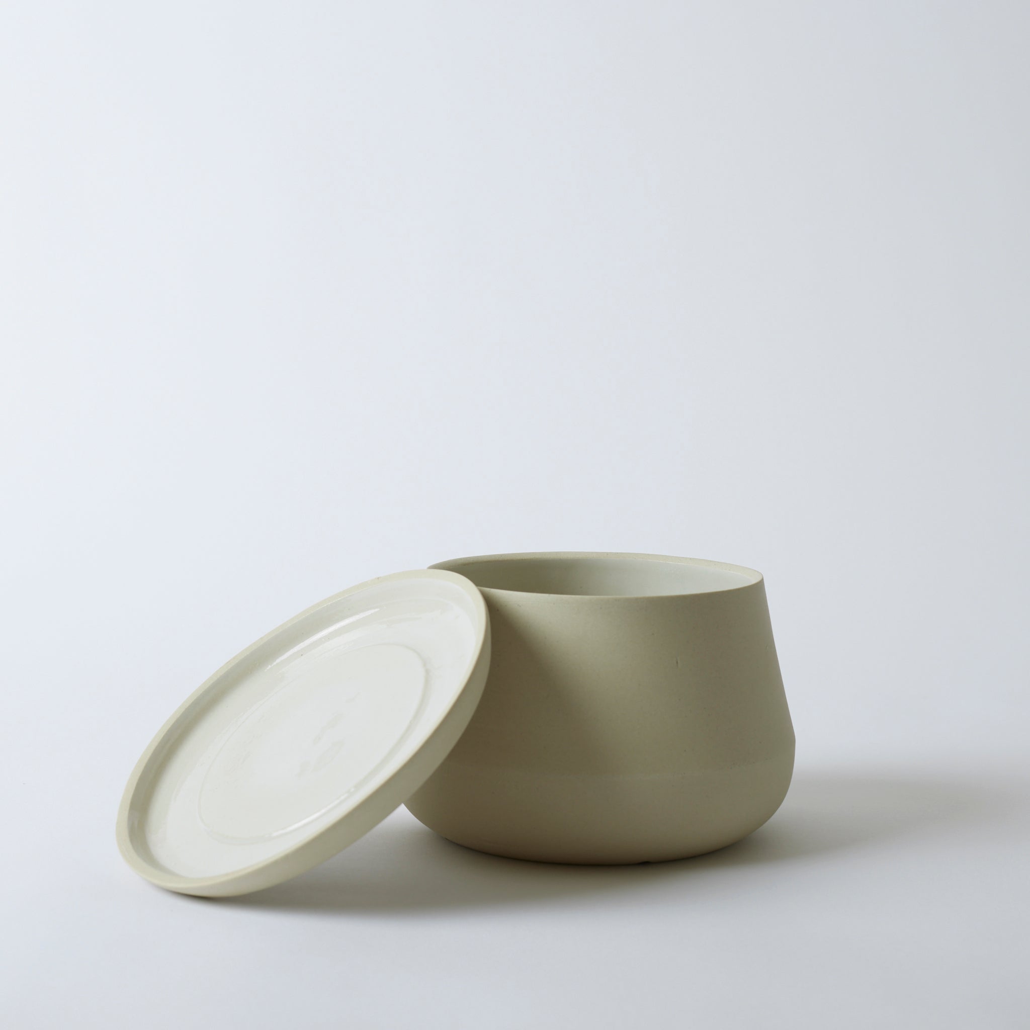 Silo image of a sand colored Rancho Planter with its saucer propped up against the pot. The saucer has a glazed top, so it is shiny.