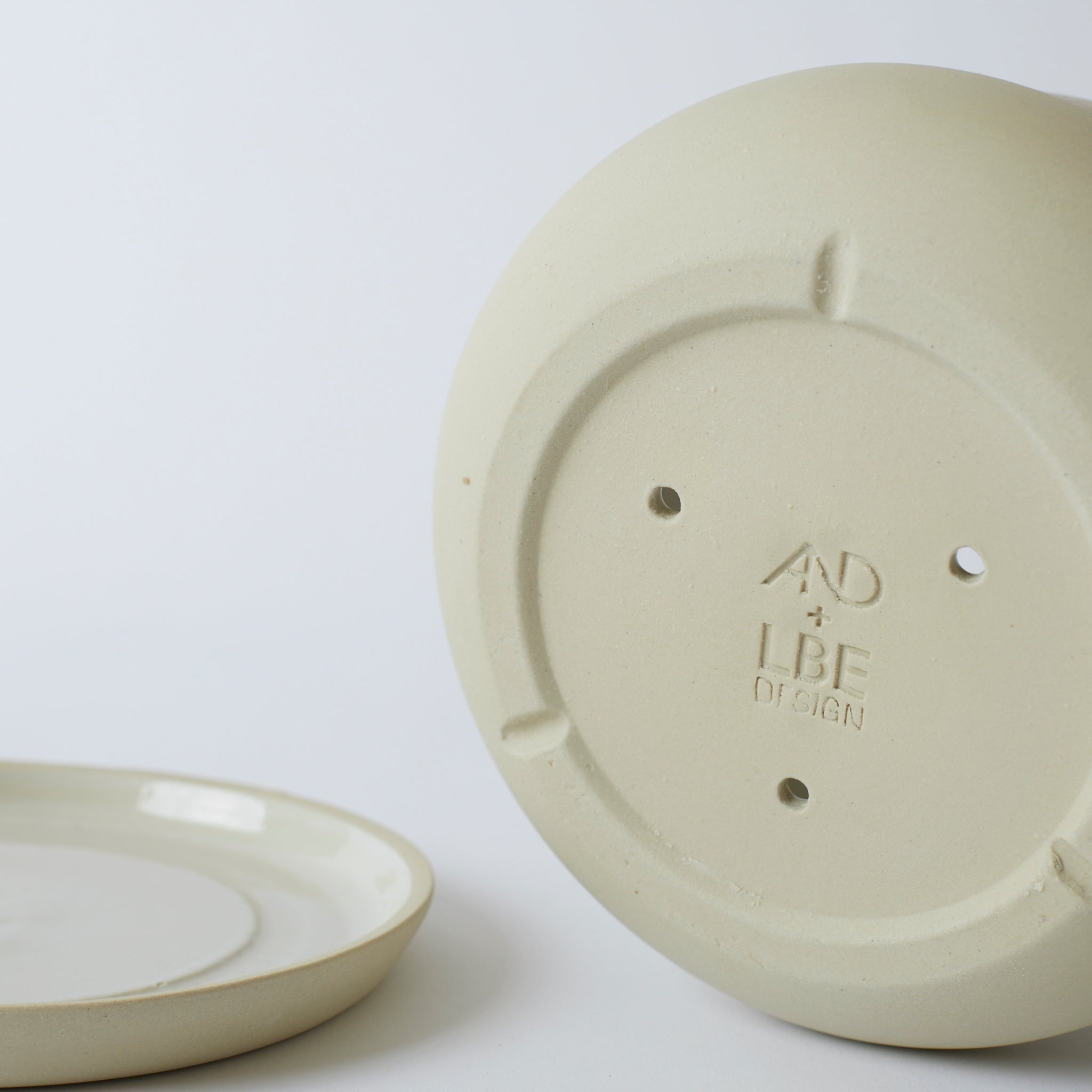 Silo photo of a sand colored Rancho Planter, showing the bottom of the pot, which has drainage holes and a stamped LBE Design logo.