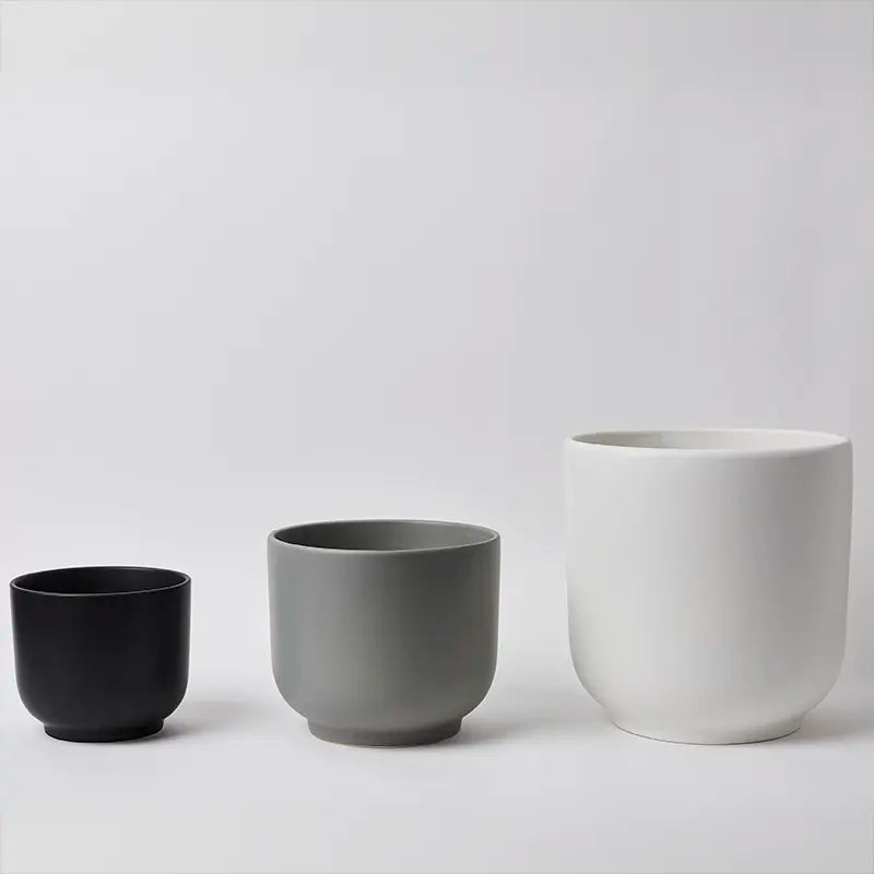 Three ceramic pots in black, gray, and white on a light gray background